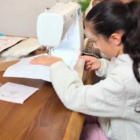 8jährige näht konzentriert an der Nähmaschine 480x480 Mädchen näht alleine eine cuci cuci-Nähvorlage an einer Nähmaschine, die auf einem Wohnzimmertisch steht