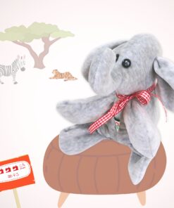 Der Elefant Fantino sitzt als fertiggenähtes Kuscheltier auf einem braungezeichneten Hocker. Im Hintergrund sieht man ebenfalls im safarilookgezeichnet einen Baum, ein Zebra und einen Tiger.