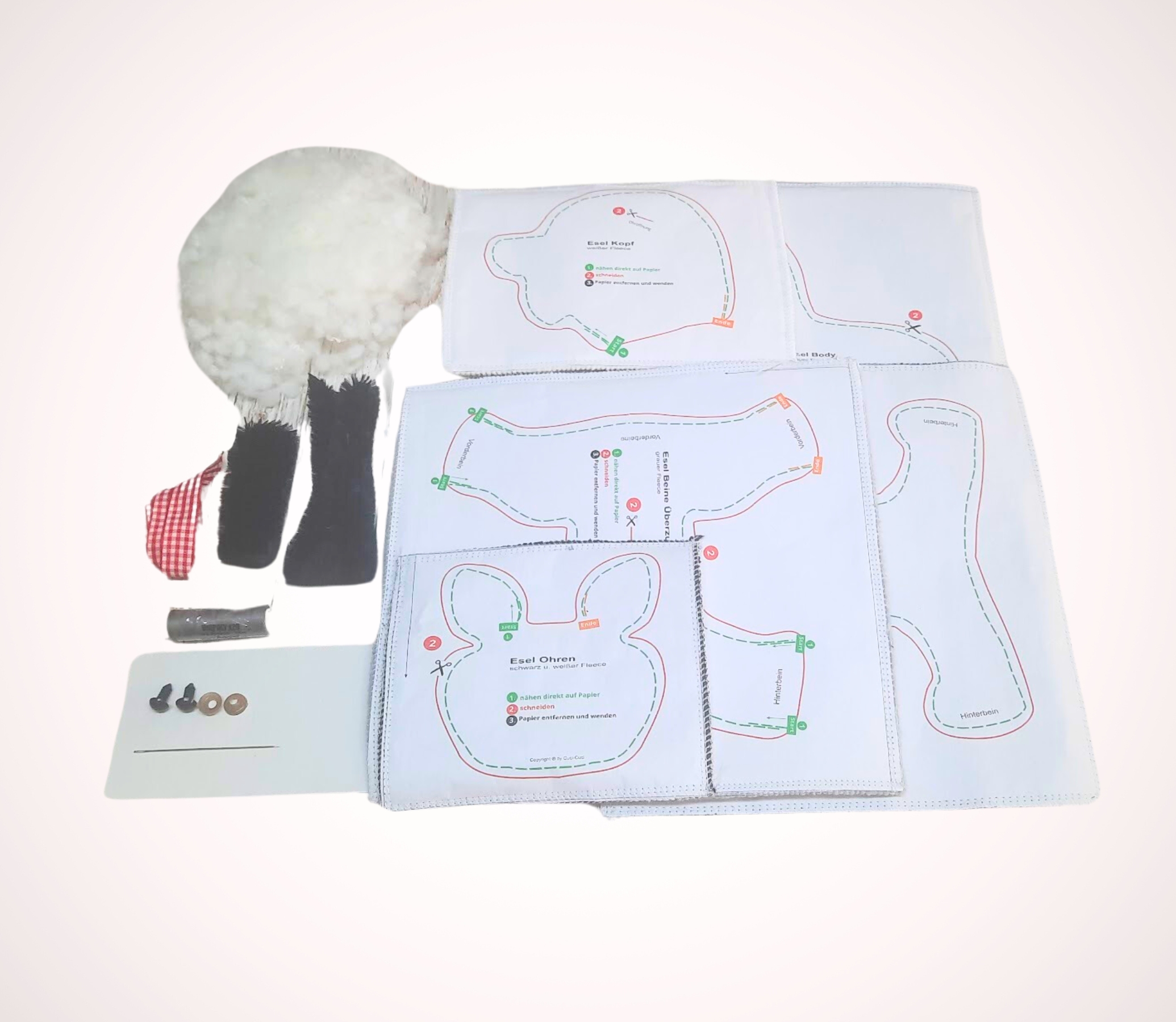 Paketinhalt von cuci cuci DIY Esel zum Selbernähen mit Nähanleitung, Füllwatte, grauem Kuschelstoff, einem rot-weiß-karierten Dekoband, Garn, Augen und einer Handnähnadel