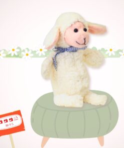 Das Schaf Peccorello sitzt als fertiggenähtes Kuscheltier auf einem graugezeichneten Hocker. Im Hintergrund sieht man eine gezeichnete Blumengirlande.