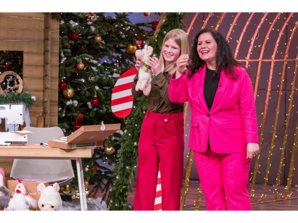 sarah-u-gruenderin-tina-califano-dhdl-bild-von-credit-rtl-bernd-michael-maurer-1-980x735.png Sara und cuci cuci-Gründerin Tina Califano pitchen in der Dezember-Ausgabe 2024 "Die Höhle der Löwen", das Aufnahmestudio ist weihnachtlich geschmückt und Sara hält ein fertig genähtes Kuscheltier in Händen.