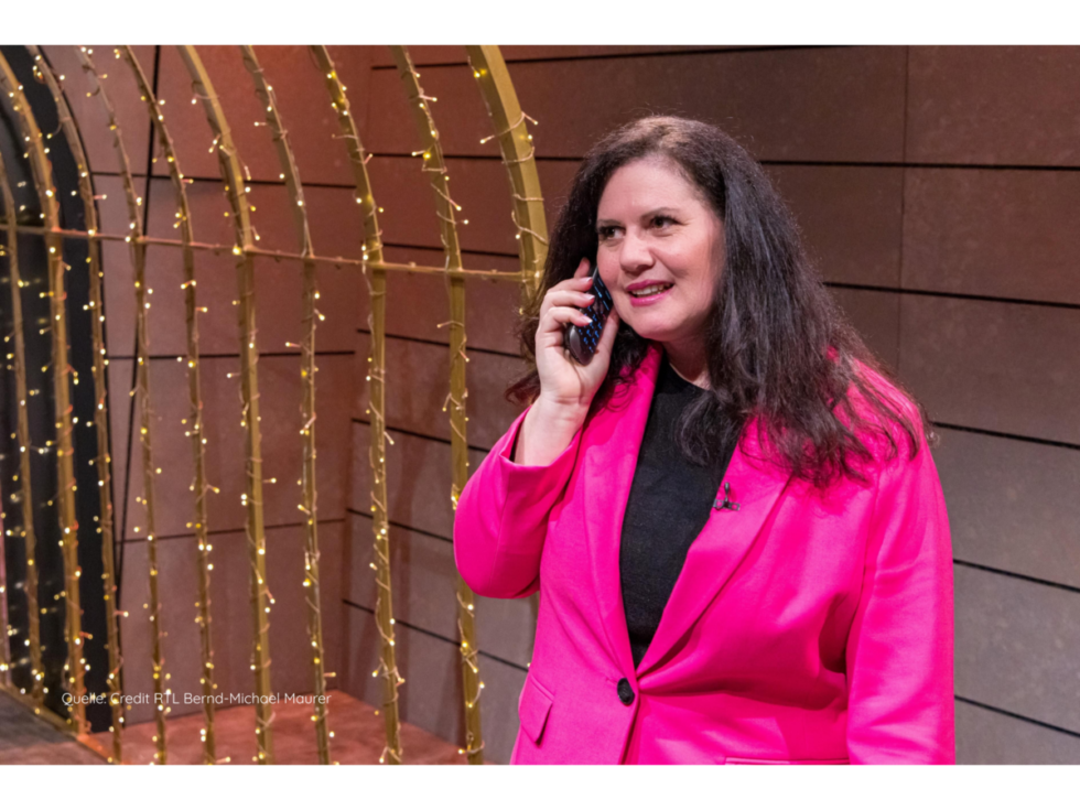 tina-califano-cuci-cuci-dhdl-bild-von-credit-rtl-bernd-michael-maurer-1-980x735.png Die in einen rosafarbenen Hosenanzug gekleidete Gründerin Tina Califano berät sich bei "Die Höhle der Löwen" vor dem mit einer Lichterkette geschmückten Löwenkäfig telefonisch mit ihrer Coachin.